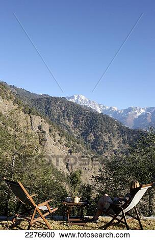 Stock Image - A tourist sits with a view of the Indian Himalayas; Uttaranchal, India. Fotosearch