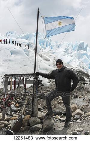 A tourist stands with a flag of Argentina as tourists hike on Moreno Glacier in the background; Santa Cruz Province, Argentina View Large Photo Image Stock Image - A tourist stands with a flag of Argentina as tourists hike on Moreno Glacier in the background; Santa Cruz Province, Argentina. Fotosearch