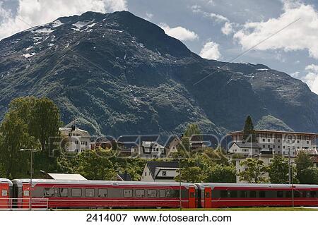 Stock Photo - A train in the foreground with a mountain, blue sky and cloud in the background of this Norway town; Andalsnes, Rauma, Norway. Fotosearch