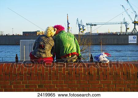 Stock Photography - A trendy couple sitting on a ledge by the river kissing; Hamburg, Germany. Fotosearch
