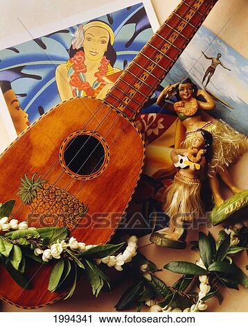 Stock Image - A ukulele with photographs and figurines of hawaiians; United States of America. Fotosearch