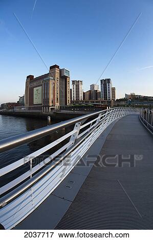 A Walking Bridge Over A River With Tall Buildings In The Distance; Gateshead Tyne And Wear England View Large Photo Image Stock Photo - A Walking Bridge Over A River With Tall Buildings In The Distance; Gateshead Tyne And Wear England. Fotosearch