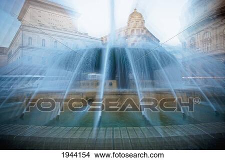 A Water Fountain Sprays Water With Buildings In The Background; Genoa Liguria Italy View Large Photo Image Picture - A Water Fountain Sprays Water With Buildings In The Background; Genoa Liguria Italy. Fotosearch