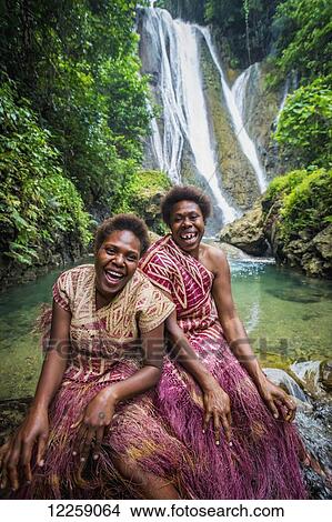 Picture - A waterfall on Tanna Island with two women in traditional costume in the foreground; Tanna Island, Vanuatu. Fotosearch