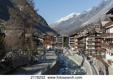 Stock Image - A Waterway Running Through The City With Pedestrians Walking On The Promenade; Zermatt Valais Switzerland. Fotosearch