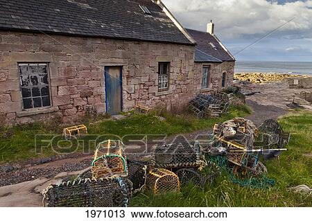 Stock Image - A Weathered Building And Lobster Traps On The Shore Along The Coast; Cove Lothian Scotland. Fotosearch