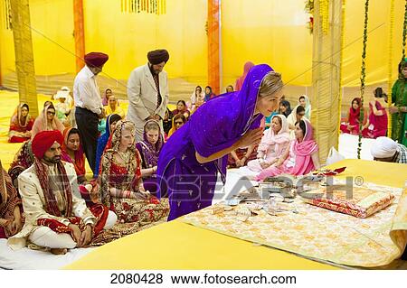 Stock Photo - A Wedding Attendant Performs A Traditional Ritual At An Indian Wedding Ceremony With The Bride And Groom Looking On; Ludhiana, Punjab, India. Fotosearch