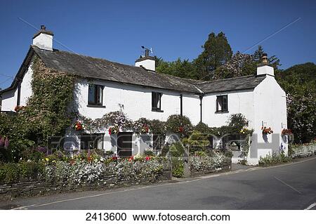 Stock Image - A white house decorated with hanging flower baskets, planters and vines; Lake District, Cumbria, England. Fotosearch