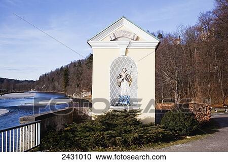 Stock Image - A white structure with a statue of a male figure along the water's edge of River Lechin; Bad Toelz, Bavaria, Germany. Fotosearch