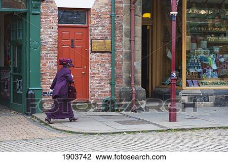 Stock Image - A Woman Dressed In Purple Walks Down The Street; Beamish, Durham, England. Fotosearch
