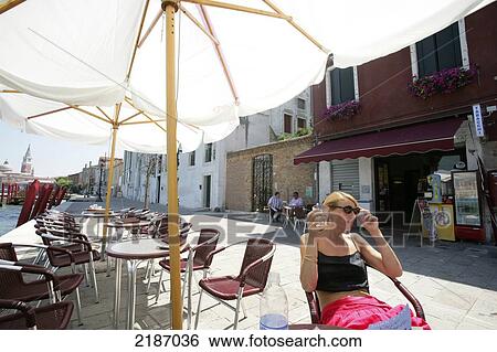Stock Photograph - A woman enjoys a drink on an outdoor patio; Venice, Italy. Fotosearch