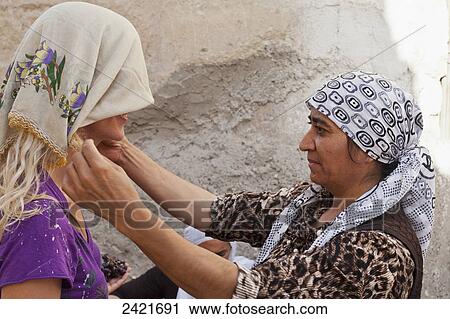 Stock Image - A woman fitting a tourist with a headscarf; Goreme, Cappadocia, Turkey. Fotosearch