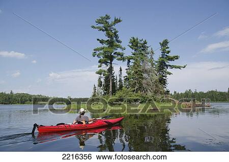Stock Photograph - A Woman In A Red Kayak On A Tranquil Lake; Lake Of The Woods Ontario Canada. Fotosearch