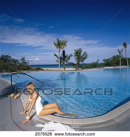 A woman in a white bathing suit sits on the edge of a swimming pool with a view of the ocean; Hawaii, United States of America View Large Photo Image Stock Photo - A woman in a white bathing suit sits on the edge of a swimming pool with a view of the ocean; Hawaii, United States of America. Fotosearch