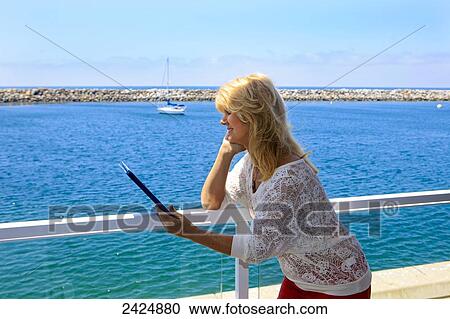 A woman in her fifties using a tablet computer by the harbor. View Large Photo Image Stock Image - A woman in her fifties using a tablet computer by the harbor.. Fotosearch
