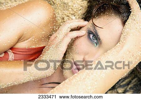 Stock Image - A woman laying in the sand with a sandy face, hair and arms; Kauai, Hawaii, United States of America. Fotosearch