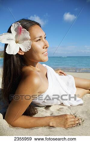 A woman laying on the beach at the water's edge with a tropical flower in her hair; Oahu, Hawaii, United States of America View Large Photo Image Stock Photo - A woman laying on the beach at the water's edge with a tropical flower in her hair; Oahu, Hawaii, United States of America. Fotosearch
