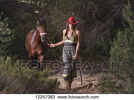 Stock Image - A woman leading her horse over a sandy trail; Tarifa, Cadiz, Andalusia, Spain. Fotosearch