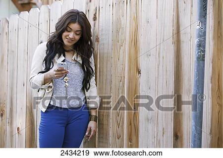 A woman leaning against a wooden fence using her cell phone; San Francisco, California, USA View Large Photo Image Stock Photo - A woman leaning against a wooden fence using her cell phone; San Francisco, California, USA. Fotosearch