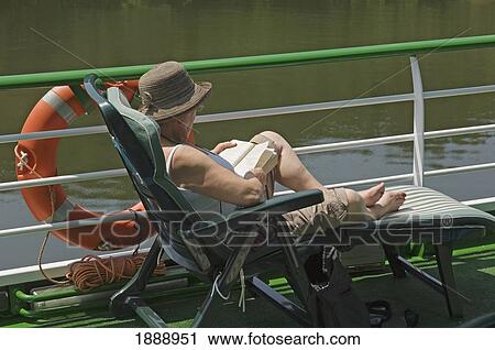 Stock Image - A Woman On A Sunlounger Reading A Book On A River Cruise. Fotosearch