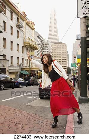 Stock Image - A woman on the side of the road hailing a cab; san francisco california united states of america. Fotosearch