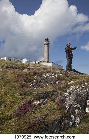 Stock Photography - A Woman Points As She Stands In Front Of Ardnamurchan Lighthouse; Ardnamurchan Argyl Scotland. Fotosearch