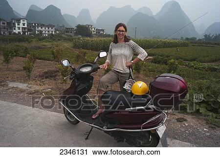 A Woman Poses With Her Motor Scooter With The Peaked Mountains In The Background; Yangshuo, China View Large Photo Image Stock Image - A Woman Poses With Her Motor Scooter With The Peaked Mountains In The Background; Yangshuo, China. Fotosearch