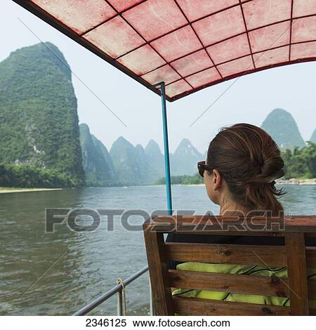 Stock Photography - A Woman Rides In A Covered Boat Down The Li River; Guilin, Guangxi, China. Fotosearch