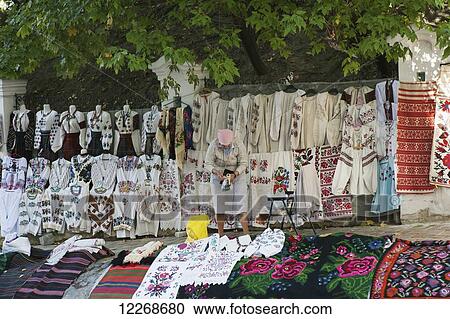Stock Image - A woman selling embroidered clothes, table cloths and rugs at a market stall on Andriyivsky uzviz; Kiev, Ukraine. Fotosearch
