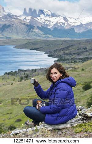 A woman sits having a drink and snack with a view of a lake and rugged mountain landscape, Torres del Paine National Park; Torres del Paine, Magallanes and Antartica Chilena Region, Chile View Large Photo Image Stock Image - A woman sits having a drink and snack with a view of a lake and rugged mountain landscape, Torres del Paine National Park; Torres del Paine, Magallanes and Antartica Chilena Region, Chile. Fotosearch