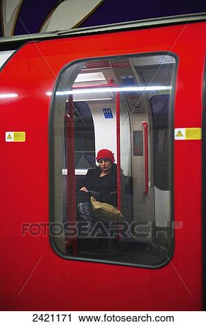 Stock Image - A woman sits inside a subway train as viewed through the window from the outside; London, England. Fotosearch
