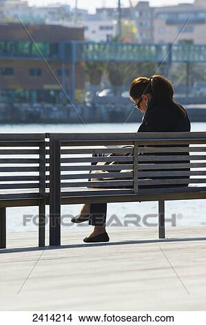 A woman sits on a bench at the water's edge; Barcelona, Spain View Large Photo Image Picture - A woman sits on a bench at the water's edge; Barcelona, Spain. Fotosearch