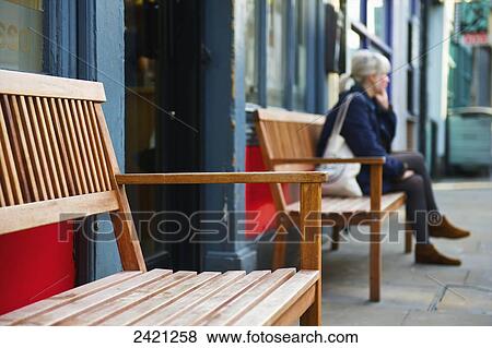 Stock Photo - A woman sits on a bench in front of a building, Shoreditch; London, England. Fotosearch