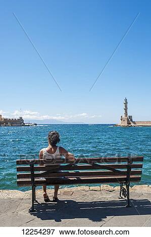 A woman sits on a bench overlooking the harbour and lighthouse; Chania, Crete, Greece View Large Photo Image Stock Photo - A woman sits on a bench overlooking the harbour and lighthouse; Chania, Crete, Greece. Fotosearch