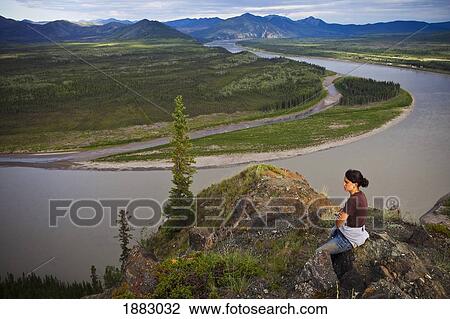 A Woman Sits On A Rock Enjoying A View Of The Yukon River; Eagle, Alaska, United States Of America View Large Photo Image Stock Image - A Woman Sits On A Rock Enjoying A View Of The Yukon River; Eagle, Alaska, United States Of America. Fotosearch