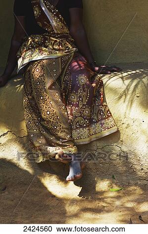 Stock Image - A woman sits on a stone ledge with bare feet; Ulpotha, Embogama, Sri Lanka. Fotosearch