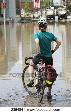 Stock Image - A Woman Sits On Her Bike Looking At The Devastation Of A Flood; Calgary, Alberta, Canada. Fotosearch