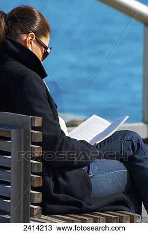 Stock Image - A woman sits reading a book at the water's edge; Barcelona, Spain. Fotosearch