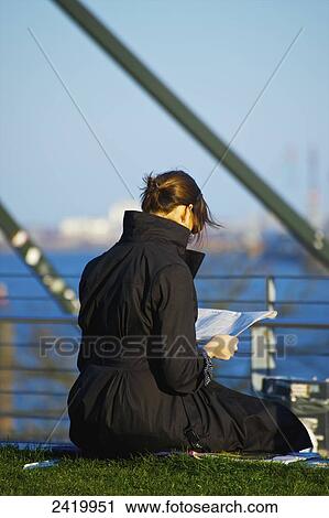 Stock Image - A woman sits reading by the water's edge; Hamburg, Germany. Fotosearch