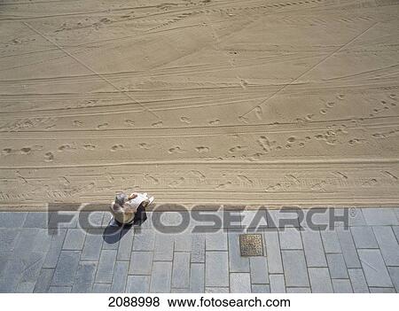 A Woman Sits Reading On A Walkway At The Edge Of The Beach View Large Photo Image Stock Photo - A Woman Sits Reading On A Walkway At The Edge Of The Beach. Fotosearch
