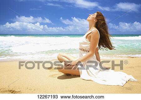 A woman sitting on the sand at the water's edge soaking up the sun; Kealia, Kauai, Hawaii, United States of America View Large Photo Image Stock Image - A woman sitting on the sand at the water's edge soaking up the sun; Kealia, Kauai, Hawaii, United States of America. Fotosearch