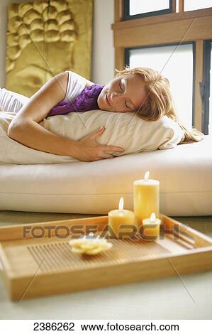 Stock Image - A woman sleeping on a bed with candles burning on a table; Hawaii, United States of America. Fotosearch