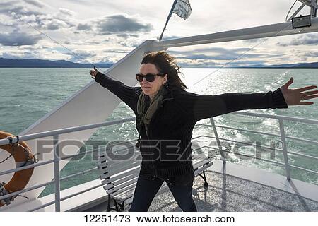 Stock Image - A woman standing with arms out against the wind at the back of a boat on a lake; Santa Cruz province, Argentina. Fotosearch