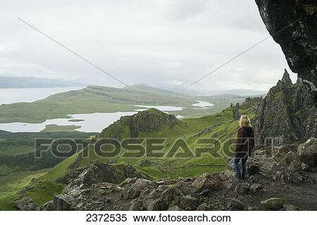 A woman stands along on a rocky ridge looking out over the landscape of hills and water; Skye, Scotland View Large Photo Image Stock Photography - A woman stands along on a rocky ridge looking out over the landscape of hills and water; Skye, Scotland. Fotosearch