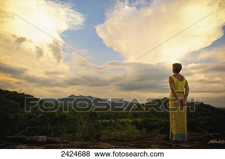 Stock Photo - A woman stands looking over the landscape at sunset; Ulpotha, Embogama, Sri Lanka. Fotosearch