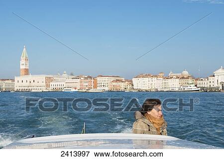 A woman stands on the back of a boat with a view of the shoreline of the Grand Canal in the distance; Venice, Veneto, Italy View Large Photo Image Stock Photo - A woman stands on the back of a boat with a view of the shoreline of the Grand Canal in the distance; Venice, Veneto, Italy. Fotosearch