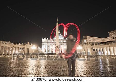 Stock Image - A woman stands with a red light trail in the shape of a heart in St. Peter's Square; Rome, Lazio, Italy. Fotosearch