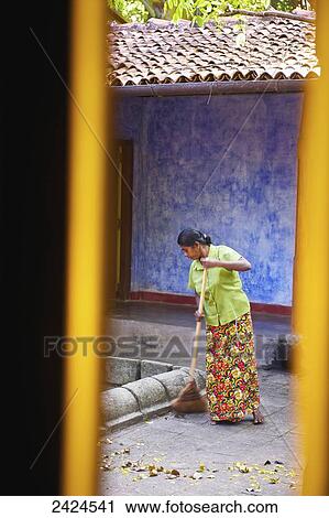Stock Image - A woman sweeping a walkway; Ulpotha, Embogama, Sri Lanka. Fotosearch