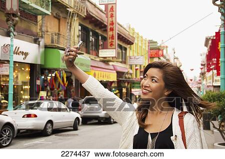 Stock Photo - A woman takes a picture of herself with her cell phone camera in a busy urban area; san francisco california united states of america. Fotosearch