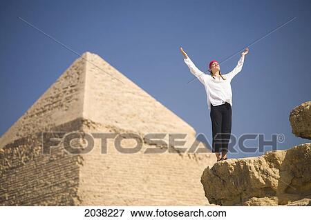 Stock Photo - A Woman Tourist Raises Her Arms In Front Of The Pyramids Of Giza Near Cairo; Giza Egypt. Fotosearch